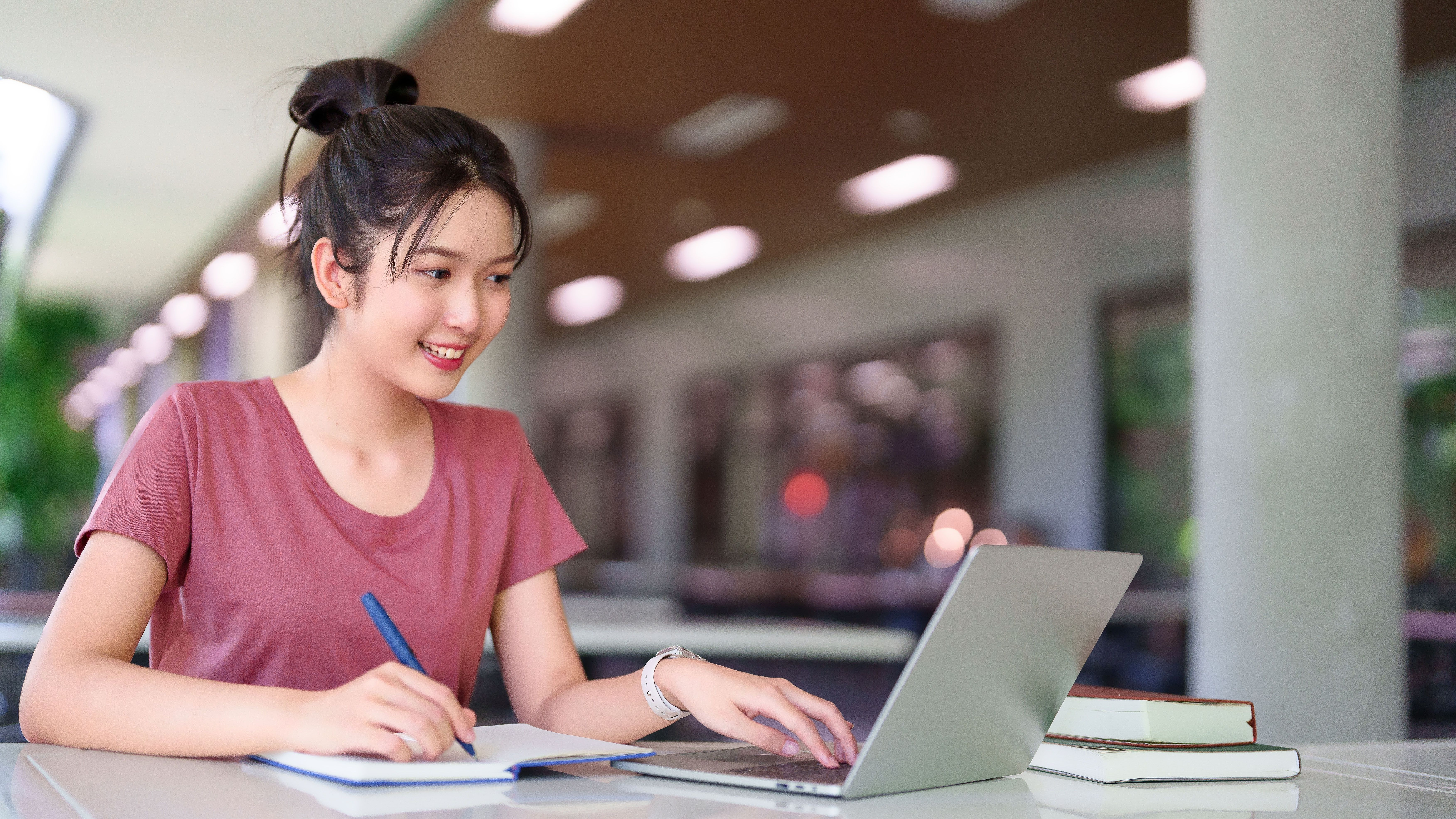 Student taking notes while working on a laptop